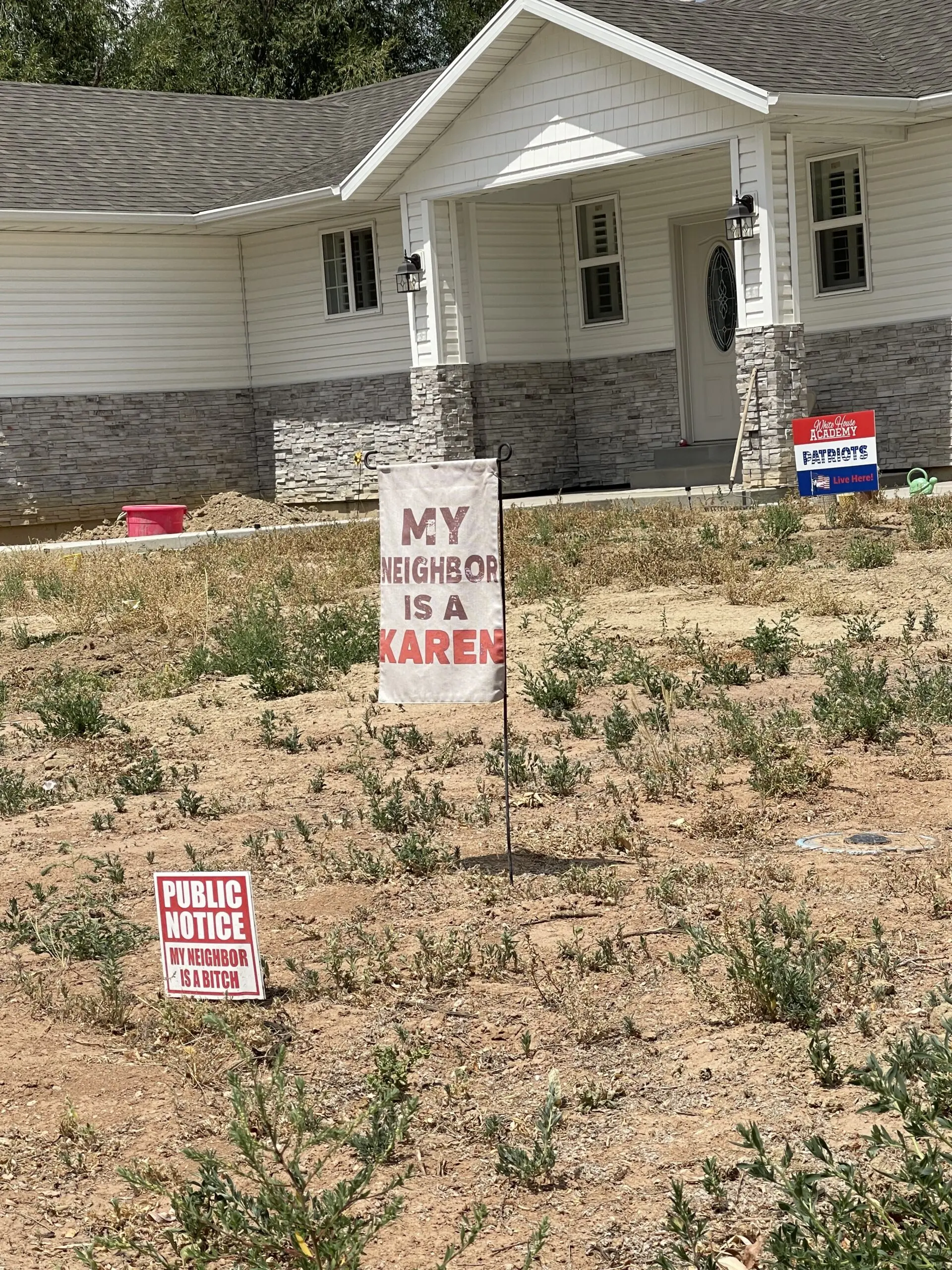Shaming signs in front of the Bloated Bully's home say "my neighbor is a Karen," "caution neighbor is a bitch" and show a sign for a local private christian school, in front of a white house with a yard full of weeds